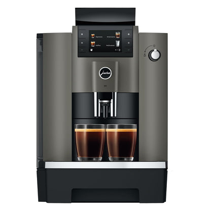 A modern automatic espresso machine in dark gray and black, shown from the front with two cups of espresso filled under the dispensing area on a white background.